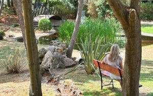 Carole Berthelot assise sur un banc dans un jardin, prenant un moment de repos et d’écoute en été